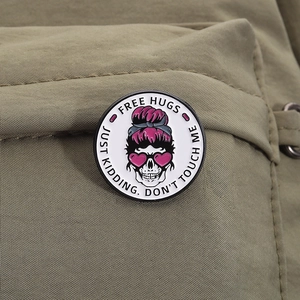Détail d'une broche crâne ronde avec texte Free Hugs sur un sac à dos en nylon vert