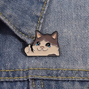 Détail d'un pin's chat mignon avec pouce levé en émail sur une veste en jean bleu