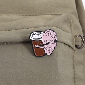 Detailed view of an enamel pin featuring a brain hugging a coffee cup on a canvas backpack
