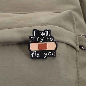 Detailed view of black enamel pin with I Will Try to Fix You text on green canvas bag