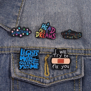 Set of 5 enamel music lyric pins on a blue denim jacket pocket featuring creative designs