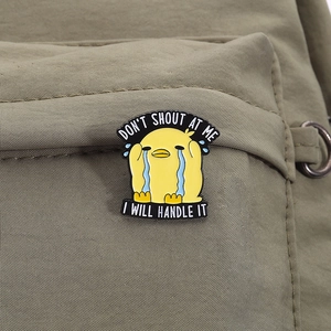 Detailed view of yellow enamel duck brooch with Don't shout at me text on green bag