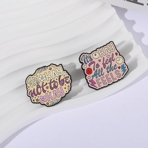 Kreative Emaille-Pins mit motivierenden Sprüchen und Blumenmotiven auf weißem Podest