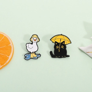 Cute cartoon enamel pins set featuring a white duck and black cat with yellow umbrellas