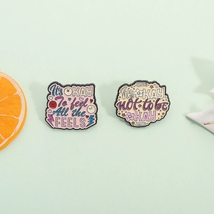 Zwei inspirierende Emaille-Pins mit motivierenden Zitaten auf einem Mint-Hintergrund