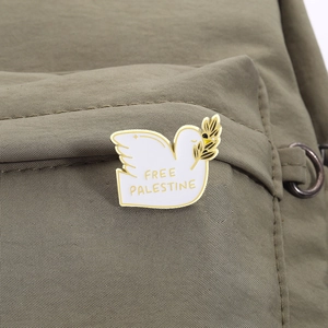 White enamel dove brooch with Free Palestine text on olive green canvas bag