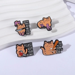 Set of 4 cute orange cat enamel pins with humorous cartoon weapon designs on display