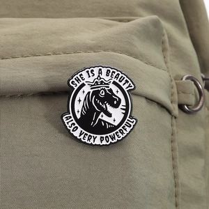 Detail of Tyrannosaurus enamel pin with crown and motivational text on green backpack