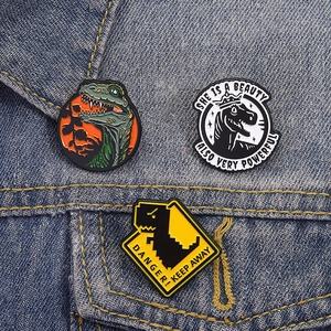 Three-piece dinosaur enamel pins set with creative letters on blue denim background