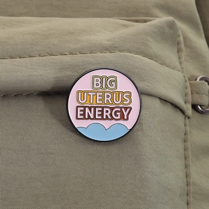 Macro shot of circular enamel brooch with Big Uterus Energy slogan on canvas bag