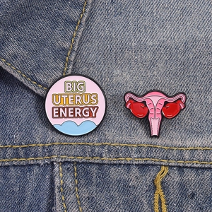 Nahaufnahme von Emaille-Pins mit Uterus-Boxhandschuh und Spruch auf Jeansstoff