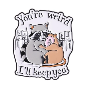 Cute raccoon and opossum enamel pin with You're weird I'll keep you text on white background