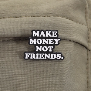 Détail macro du pin's 'MAKE MONEY NOT FRIENDS' sur un tissu texturé vert olive