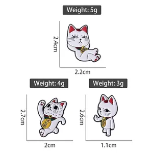 Trois pin's Maneki Neko en émail blanc avec pièces d'or et inscriptions japonaises