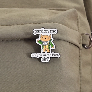 Gros plan d'un pin's chat en émail sur un sac en toile verte montrant la texture du métal