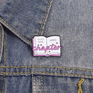 Enamel book brooch pin with Just One More Chapter quote on blue denim jacket