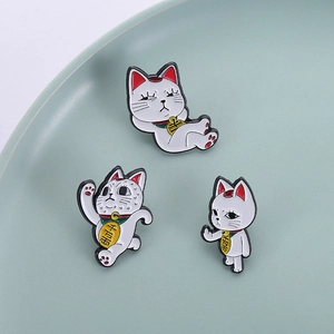 Trois broches Maneki Neko en émail avec pièces d'or sur un plateau rond bleu clair