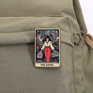 Détail macro du pin's en émail style tarot avec texte ADHD sur un sac en toile olive