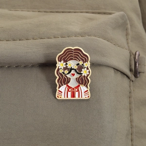 Detailed view of an enamel pin featuring a girl in sunglasses on a khaki canvas backpack