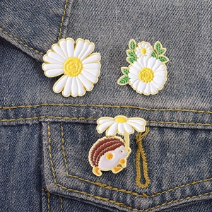 Three-piece set of daisy and hedgehog enamel pins displayed on a denim jacket pocket