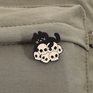 Detailed view of an enamel cat skull brooch pinned to a green canvas backpack