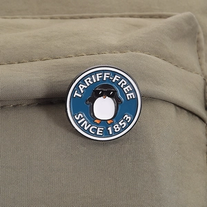Detail shot of a round enamel penguin pin with glasses on khaki fabric texture