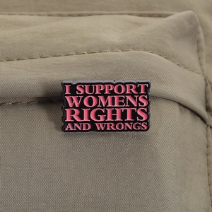 Close-up of enamel pin with feminist slogan on canvas fabric showing metallic details