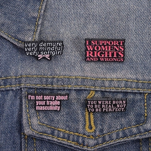 Detailed view of four enamel pins with feminist slogans on a blue denim jacket