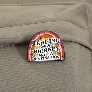 Rainbow enamel pin with healing journey quote pinned on a khaki canvas backpack