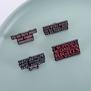 Set of four black enamel feminist quote brooches displayed on a ceramic tray