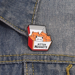 Cute kitten nuggets enamel pin on denim jacket featuring funny cartoon cat food design