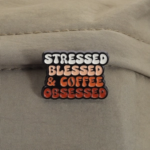 Detail of coffee slogan enamel pin on olive fabric showing vibrant text and metal edges