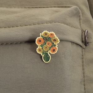 Détail macro d'une broche tournesol en émail inspirée de Van Gogh sur tissu olive