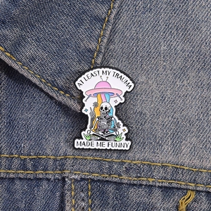 Detail of colorful UFO skeleton enamel pin on a denim jacket with funny quote engraving