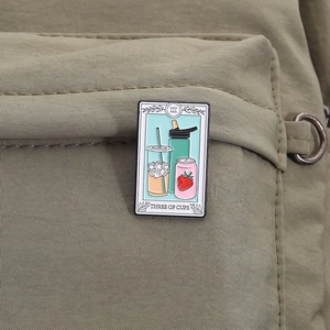 Detailed Three of Cups tarot enamel pin styled with coffee and soda on canvas bag