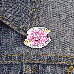Cartoon Little Miss Procrastinator enamel brooch pinned on a blue denim jacket collar
