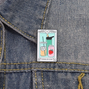Detailed view of Three of Cups tarot beverage enamel pin on a blue denim jacket collar