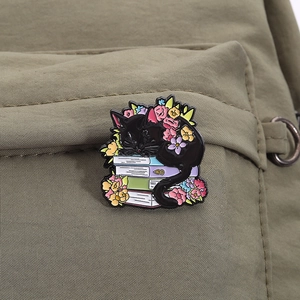 Detailed view of an enamel pin featuring a black cat sleeping on books with colorful flowers