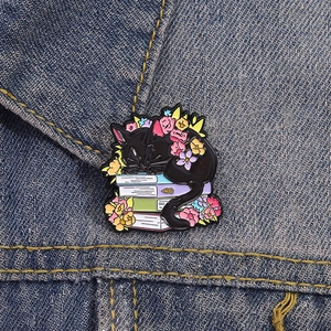 Cartoon black cat sleeping on books enamel pin badge with flowers on denim jacket