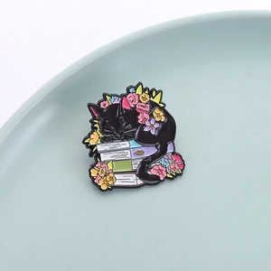 Enamel pin featuring black cat sleeping on books with flowers on light blue ceramic tray