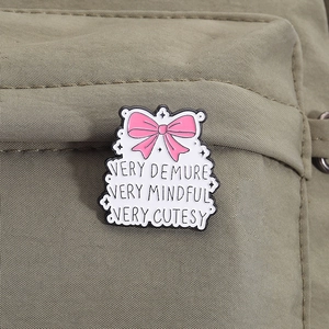 Cartoon enamel pin with pink bow and very demure text on olive canvas bag