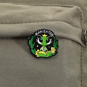 Detail of cartoon mantis enamel pin with MAN EATER text on an olive green nylon bag