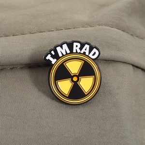 Macro detail of 'I'M RAD' radiation sign enamel pin on an olive green fabric background