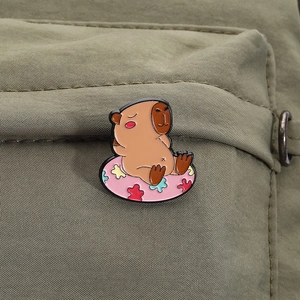 Detail view of a cute capybara enamel pin in a floral floatie on olive green fabric