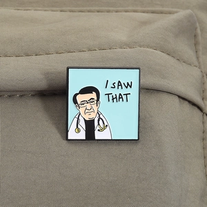 Detail of square enamel pin featuring cartoon Dr. Now with I SAW THAT quote on fabric