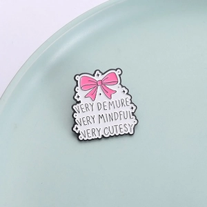 Pink bow enamel pin with slogan VERY DEMURE VERY MINDFUL on a minimalist ceramic plate
