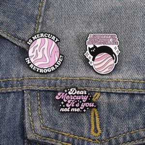 Detailed view of three purple enamel pins pinned on a blue denim jacket pocket