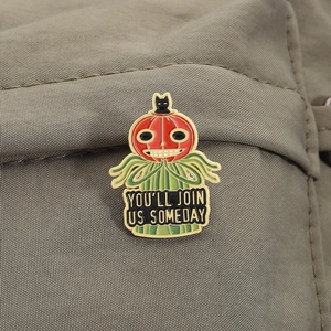 Detail of Jack O'Lantern ghost enamel pin with black cat on textured fabric surface