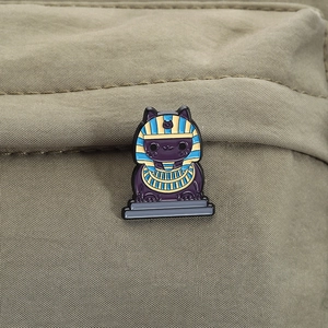 Detailed close-up of a purple Egyptian cat enamel pin styled on an olive canvas bag