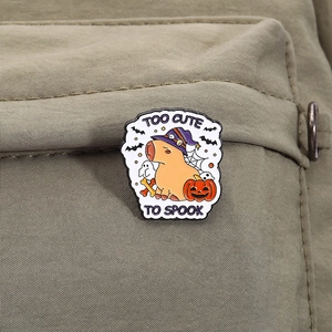 Detail of Halloween capybara enamel pin with Too Cute To Spook text on a khaki backpack